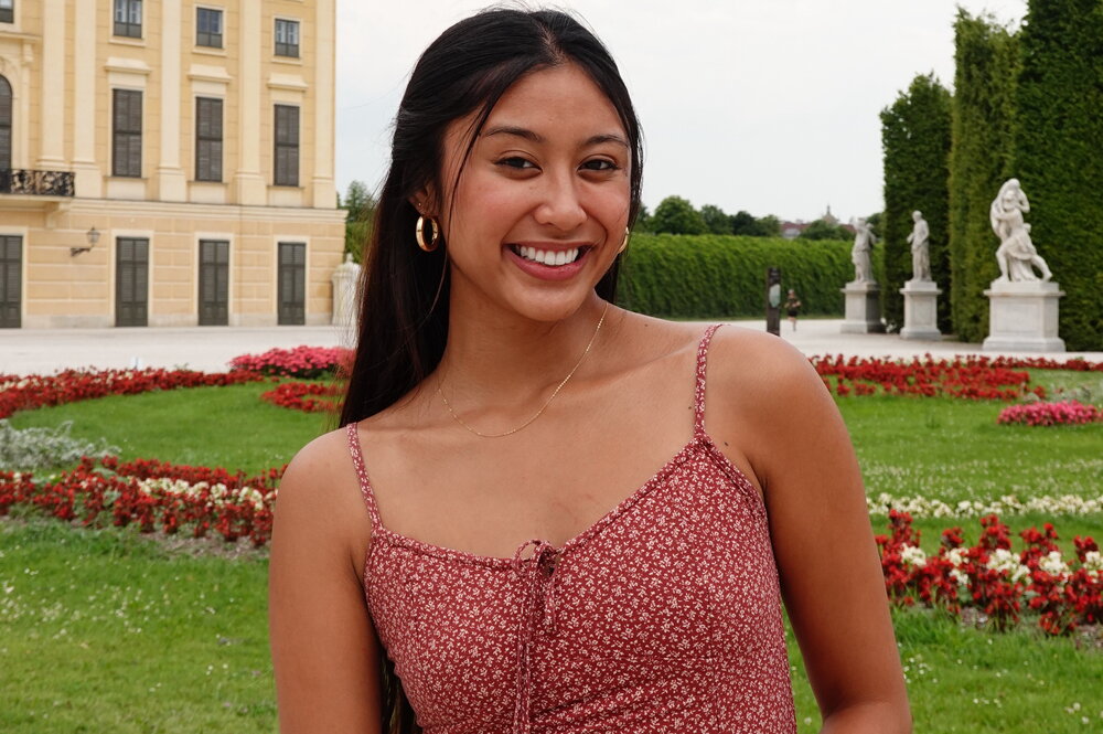 A photo of a woman in a pink dress with a grassy garden and a building behind her
